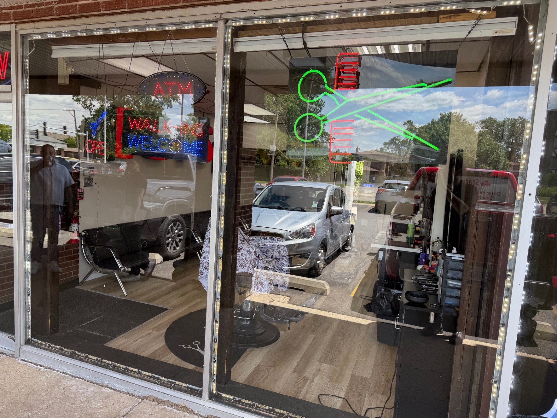 Walk-ins Welcome neon sign in the shop window with barber chairs behind it